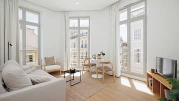 A modern living room with a sofa, chairs, a small table, and a TV.