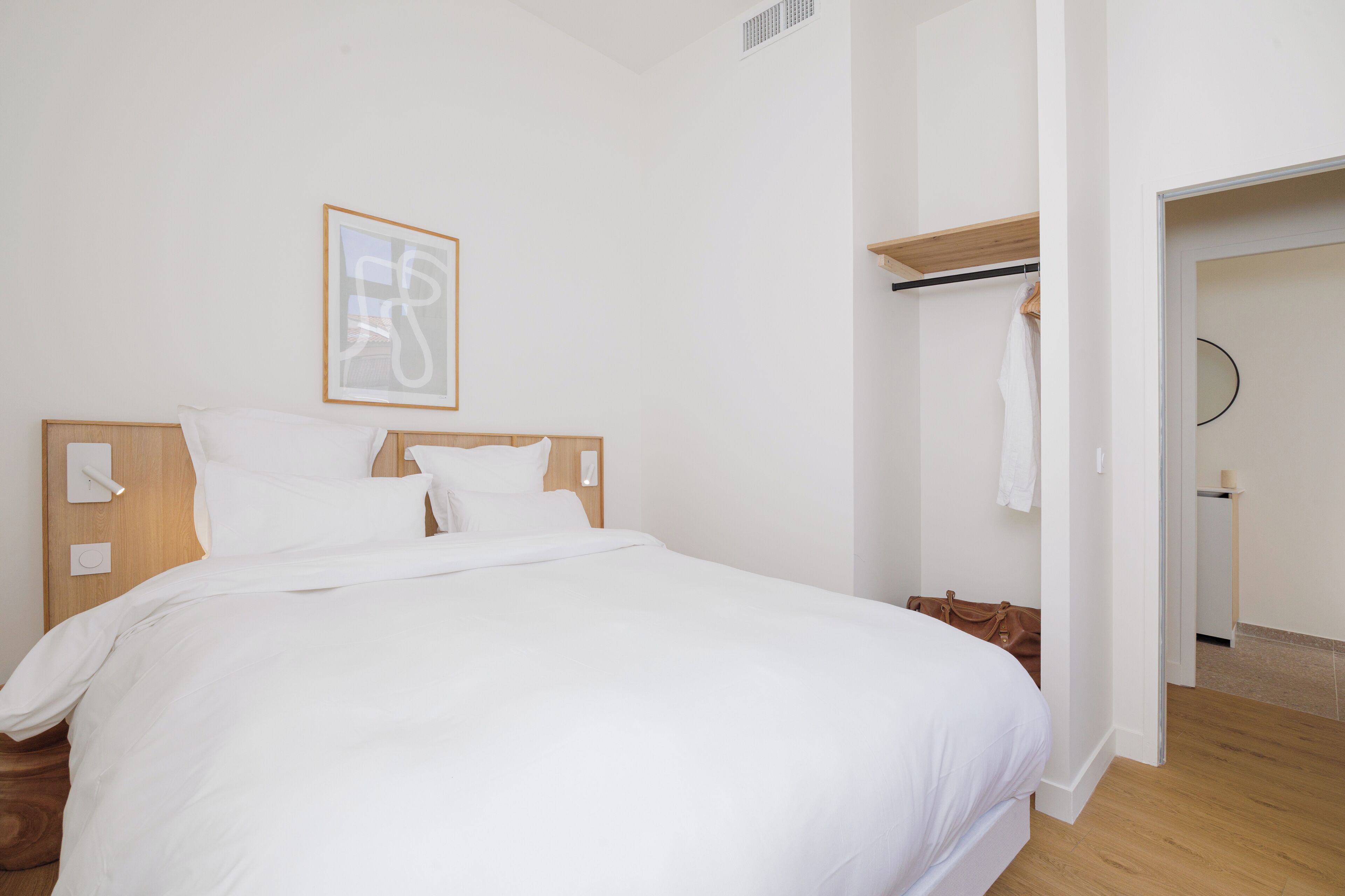 Habitación de hotel con una cama grande, cabecera de madera, mesita de noche, lámpara de pared e imagen enmarcada.