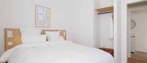 A hotel room with a large bed, a wooden headboard, a bedside table, a wall-mounted light, and a framed picture.