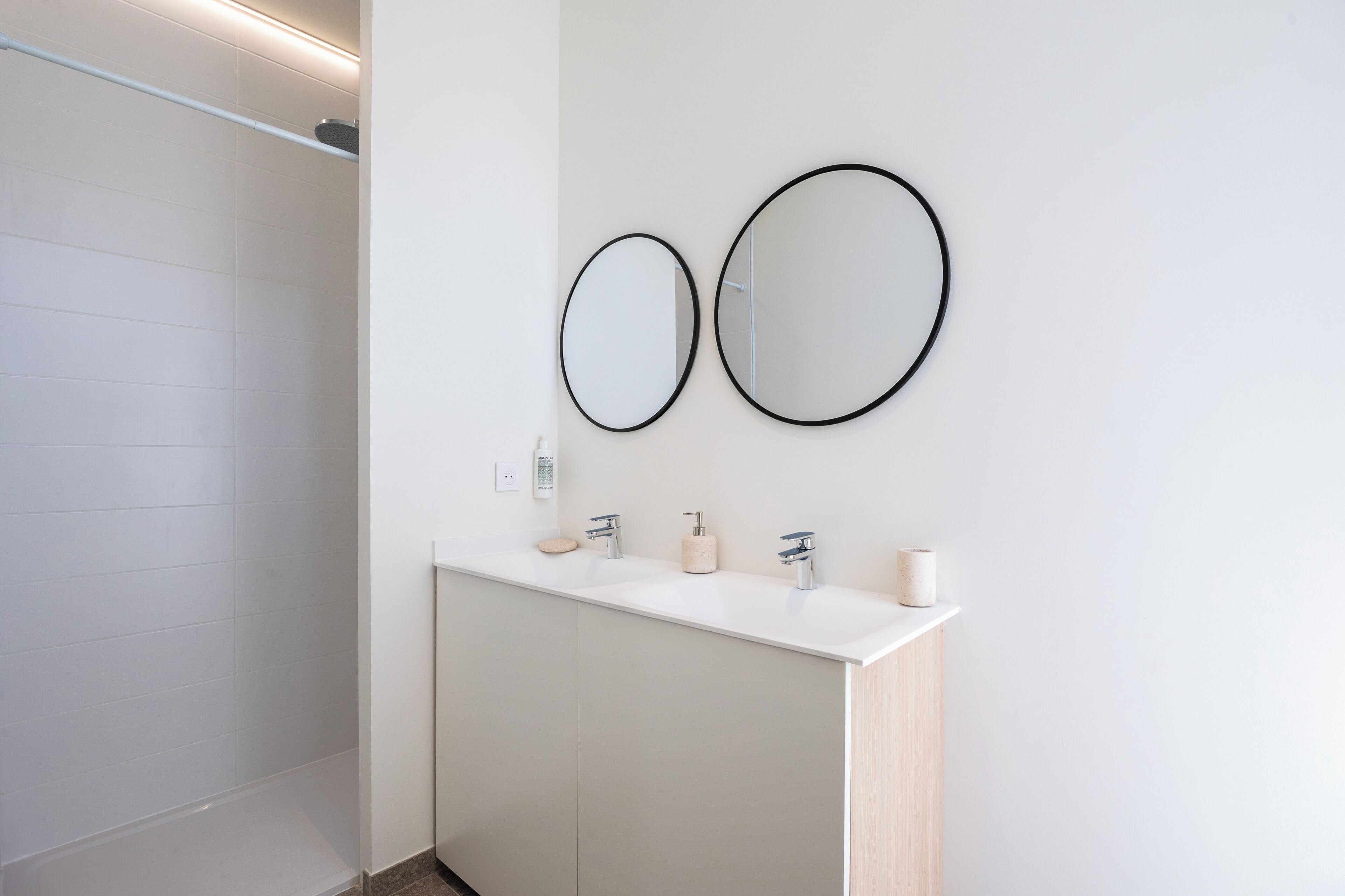 A modern bathroom with a white vanity, two wall-mounted mirrors, a shower, and a toilet.