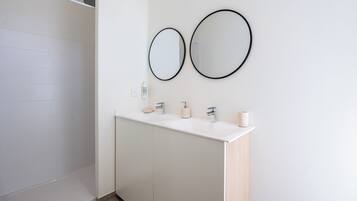 A modern bathroom with a white vanity, two wall-mounted mirrors, a shower, and a toilet.
