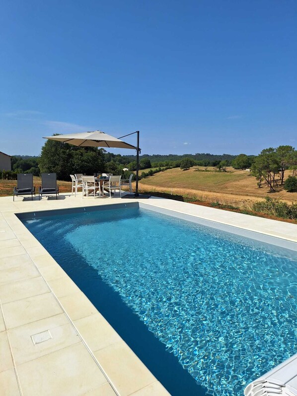 Une piscine rectangulaire Ă lâeau dâun bleu limpide, entourĂ©e dâune terrasse carrelĂ©e.