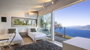 Een moderne slaapkamer met een groot raam, twee bedden, een bureau en uitzicht op zee.