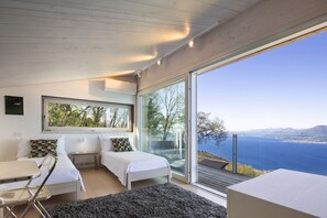 A modern bedroom with a large window, two beds, a desk, and a view of the sea. - Villa Bella with Lake View (San Zeno di Montagna)
