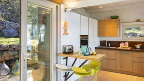 Een moderne keuken met een glazen deur naar een patio, houten kasten, een ingebouwde oven en een kleine eethoek met stoelen.