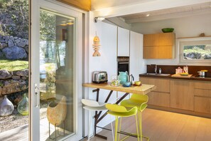 A modern kitchen with a glass door leading to a patio, wooden cabinets, a built-in oven, and a small dining area with chairs. - Villa Bella with Lake View (San Zeno di Montagna)