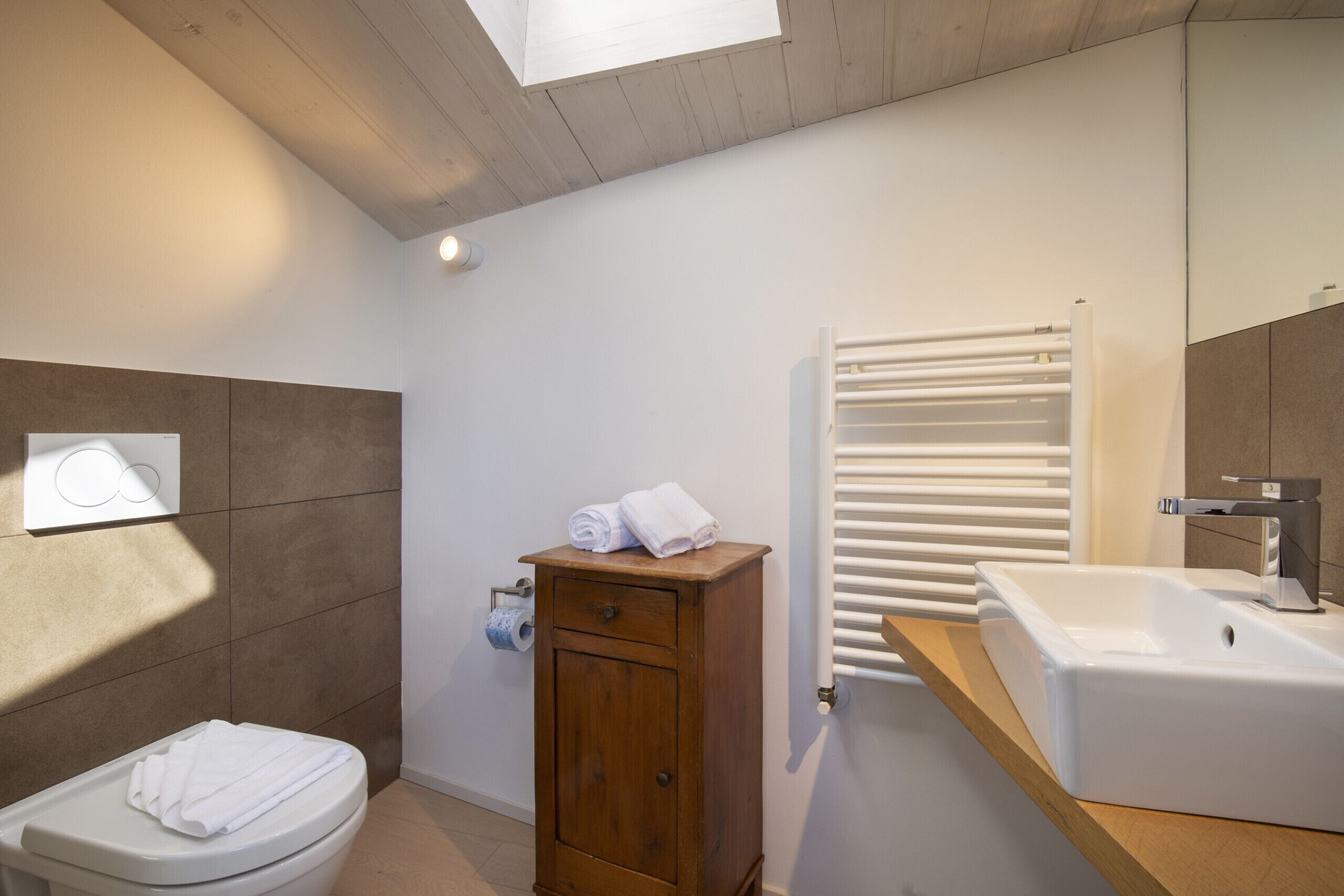 A modern bathroom with a toilet, wooden cabinet, white sink, and a towel rack.