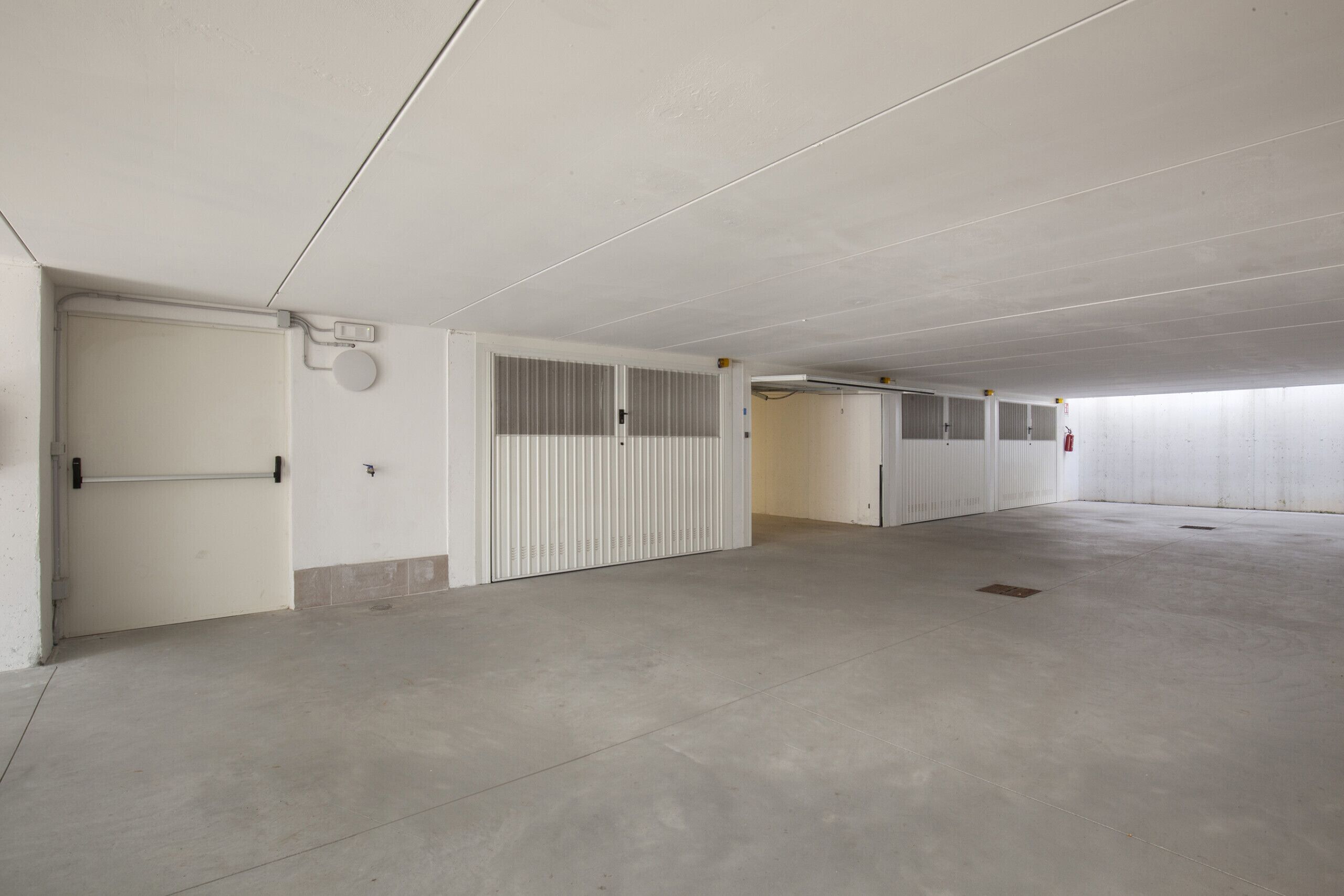 Un vaste parking souterrain, vide, avec des planchers en béton et des murs blancs.