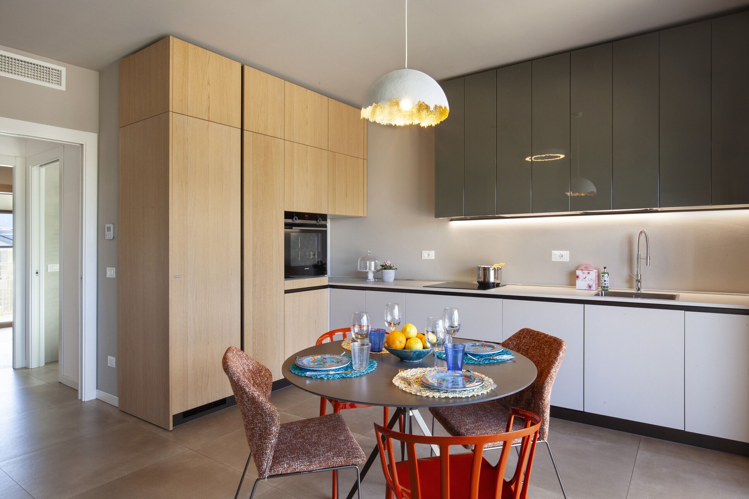 Una cocina moderna con armarios de madera, una mesa de comedor con sillas e iluminación colgante.