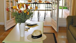 A room with a dining table, chairs, a vase with flowers, a hat, and a window with a view of greenery. - Var Duplex House for 6 With Pool (Fayence)