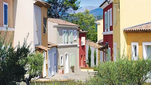 A narrow street with buildings on either side, a tree in the center, and a mountain in the background. - Var Duplex House for 6 With Pool (Fayence)