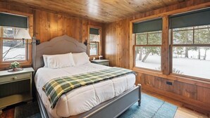 Une chambre à coucher aux murs lambrissés, avec un lit, des tables de chevet et de grandes fenêtres.