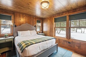 Ein Schlafzimmer mit Holzwänden, einem Bett, Nachttischen und großen Fenstern.