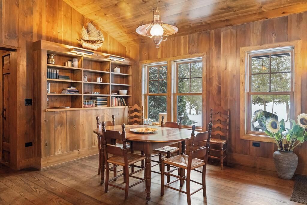 Un intérieur en bois comprenant une table à manger, des chaises, une bibliothèque et une grande fenêtre.