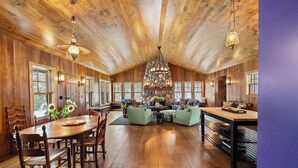 Une pièce spacieuse avec un plafond en bois, une cheminée en pierre et un coin repas comprenant une table et des chaises en bois.