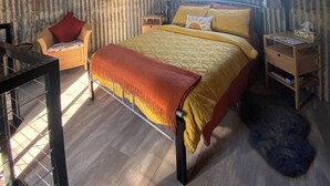 Ein Zimmer mit Bett, Sessel, kleinem Tisch und Fenster.