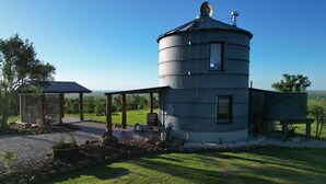 Ein großer, zylindrischer Wasserturm mit überdachtem Außenbereich, einer kleinen Holzkonstruktion und einem Rasenfeld.