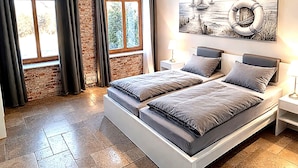 A modern bedroom with a brick wall, a large bed, a painting of sailboats, and a view through the window. - Landliche Auszeit fur die Ganze Familie (Fehmarn)