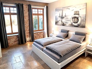 A modern bedroom with a brick wall, a large bed, a painting of sailboats, and a view through the window. - Landliche Auszeit fur die Ganze Familie (Fehmarn)