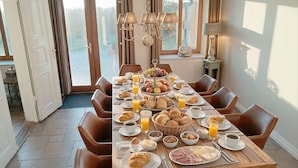 A dining table set with breakfast items, surrounded by chairs, in a room with large windows and a chandelier. - Landliche Auszeit fur die Ganze Familie (Fehmarn)