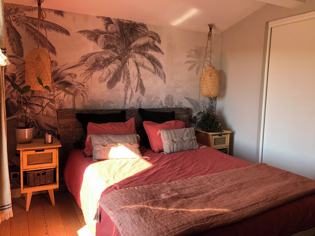 Een slaapkamer met een bed, een muurschildering, een hanglamp en een nachtkastje.