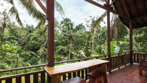 A wooden deck with a table and benches overlooking a lush tropical forest.