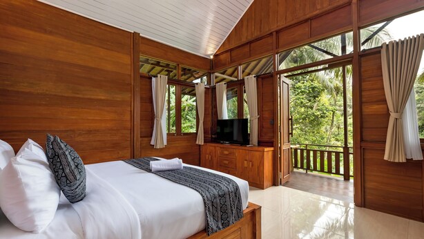 A wooden room with a bed, TV, and balcony with curtains.