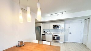 A modern kitchen with stainless steel appliances, a wooden dining table, and pendant lighting. - 2BR High-Floor Suite · Waterway Views (Hallandale Beach)