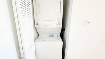 A white washing machine in a small, enclosed laundry area with a door and a wall-mounted light switch.