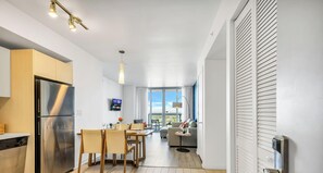 A modern kitchen with a stainless steel refrigerator, dining table with chairs, and a TV mounted on the wall. - 2BR High-Floor Suite · Waterway Views (Hallandale Beach)