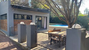 A modern outdoor seating area with a pool, enclosed by a fence and featuring a bench and table. - 46 on Allcock Guest Apartment & Suite (Pretoria)