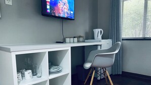 A modern room with a white desk, a chair, a television mounted on the wall, and a window with blinds. - 46 on Allcock Guest Apartment & Suite (Pretoria)