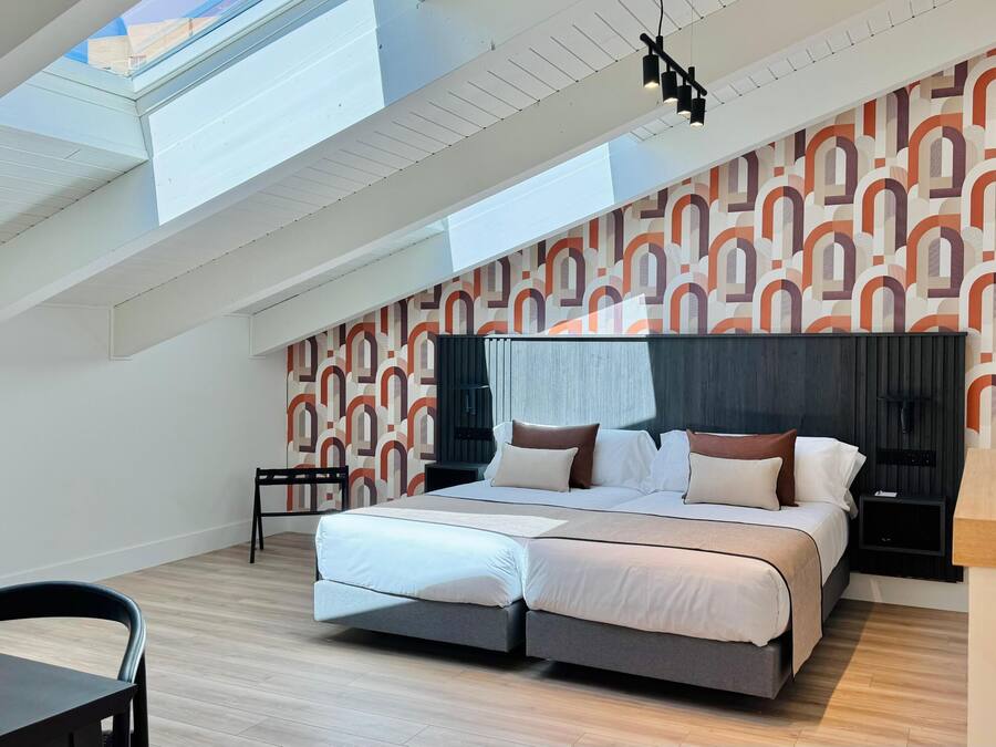 Ein modernes Schlafzimmer mit Dachfenster, einem Bett mit vielen Kissen, einem Nachttisch und einer Wand mit Muster.