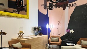 A modern interior with a reception desk, seating area, and a large wall with a 'S' logo. - Soho Boutique La Harinera (Valladolid)