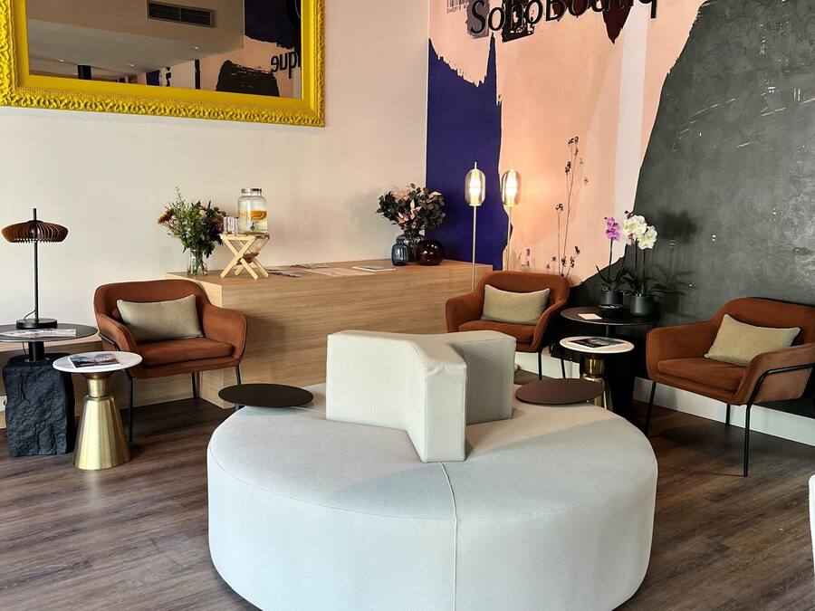 A modern lounge area with a round white sofa, two brown armchairs, a small coffee table, and a decorative mirror.