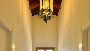 A narrow hallway with a chandelier, two white chairs, a round table, and a window with a view. - Soho Boutique La Harinera (Valladolid)