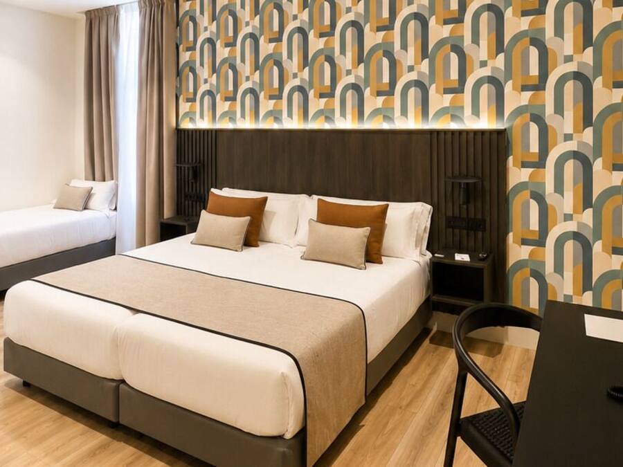 A hotel room with a large bed, a smaller bed, a desk with a phone, and a patterned wall.