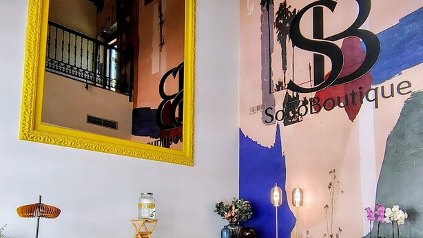 A modern living room with a large mirror, a sofa, a coffee table, and a decorative wall with a logo. - Soho Boutique La Harinera (Valladolid)