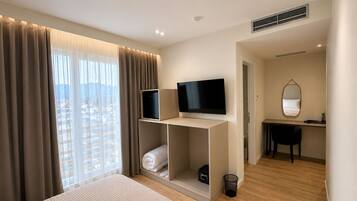 A modern hotel room with a bed, a TV, a desk, and a view of the city.