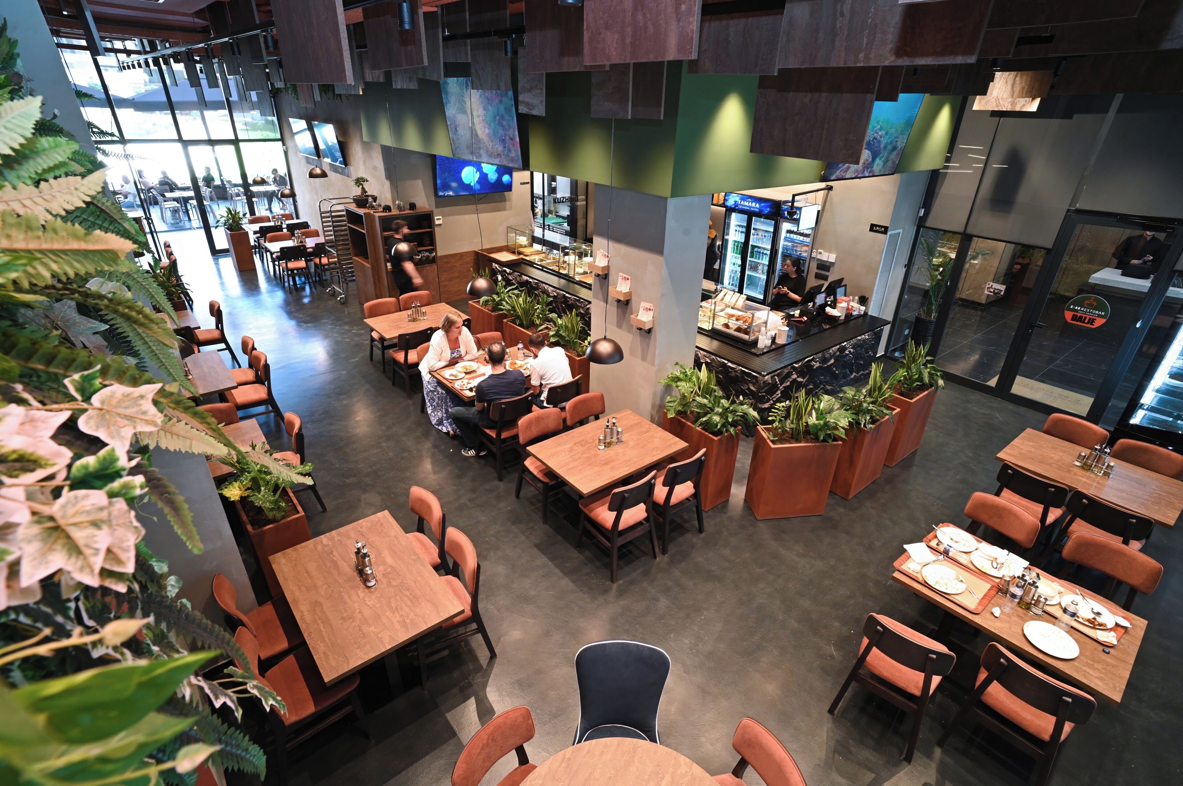 Un restaurant doté de plusieurs tables et chaises, de plantes en pot et d’un espace bar.