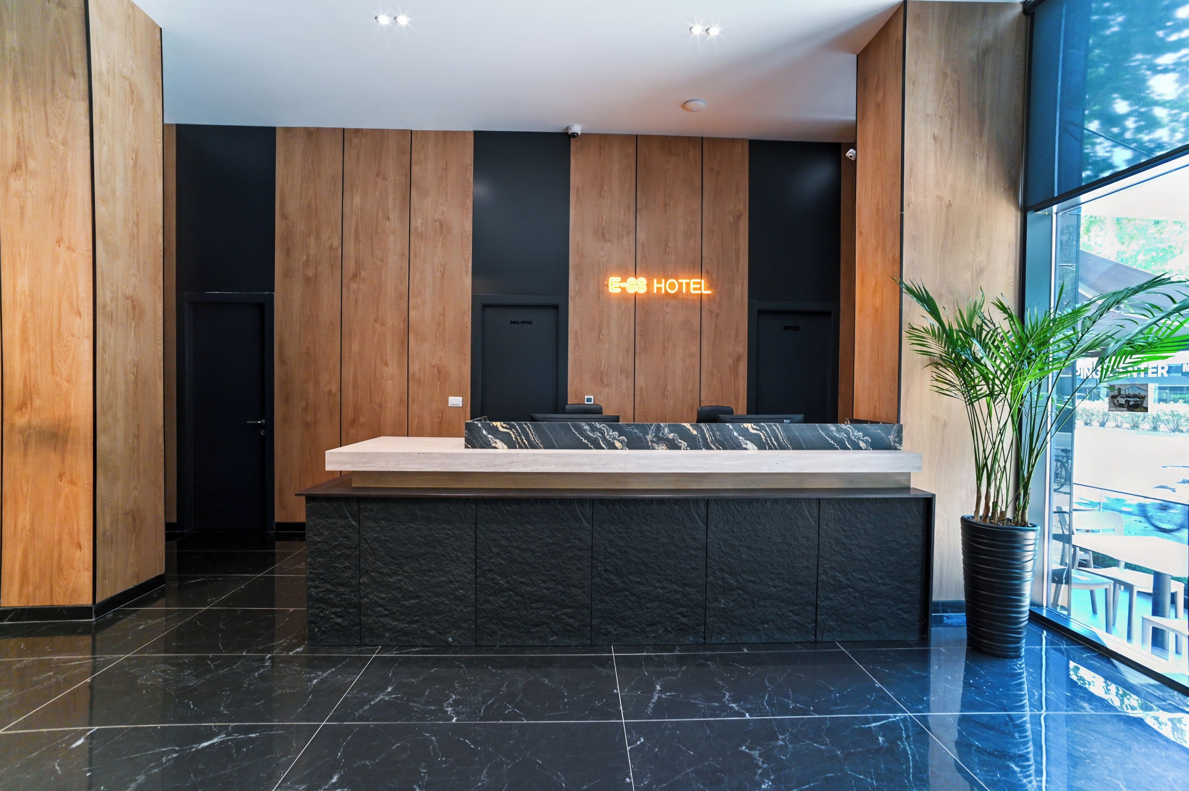 A hotel reception area with a marble reception desk, wooden panel walls, and a large potted plant.