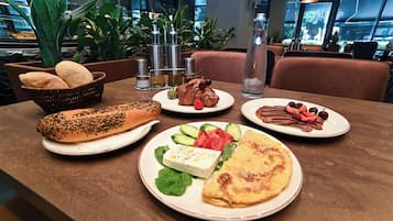 A dining table with various food items, including bread, a croissant, a plate with cheese and vegetables, and a plate with chocolate and fruit.