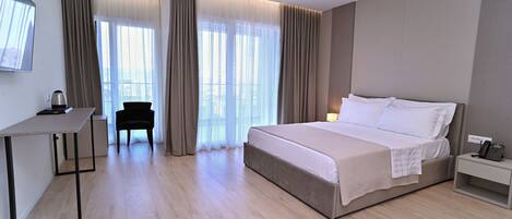 A modern hotel room with a large bed, a desk, a chair, and a bedside table with a phone.