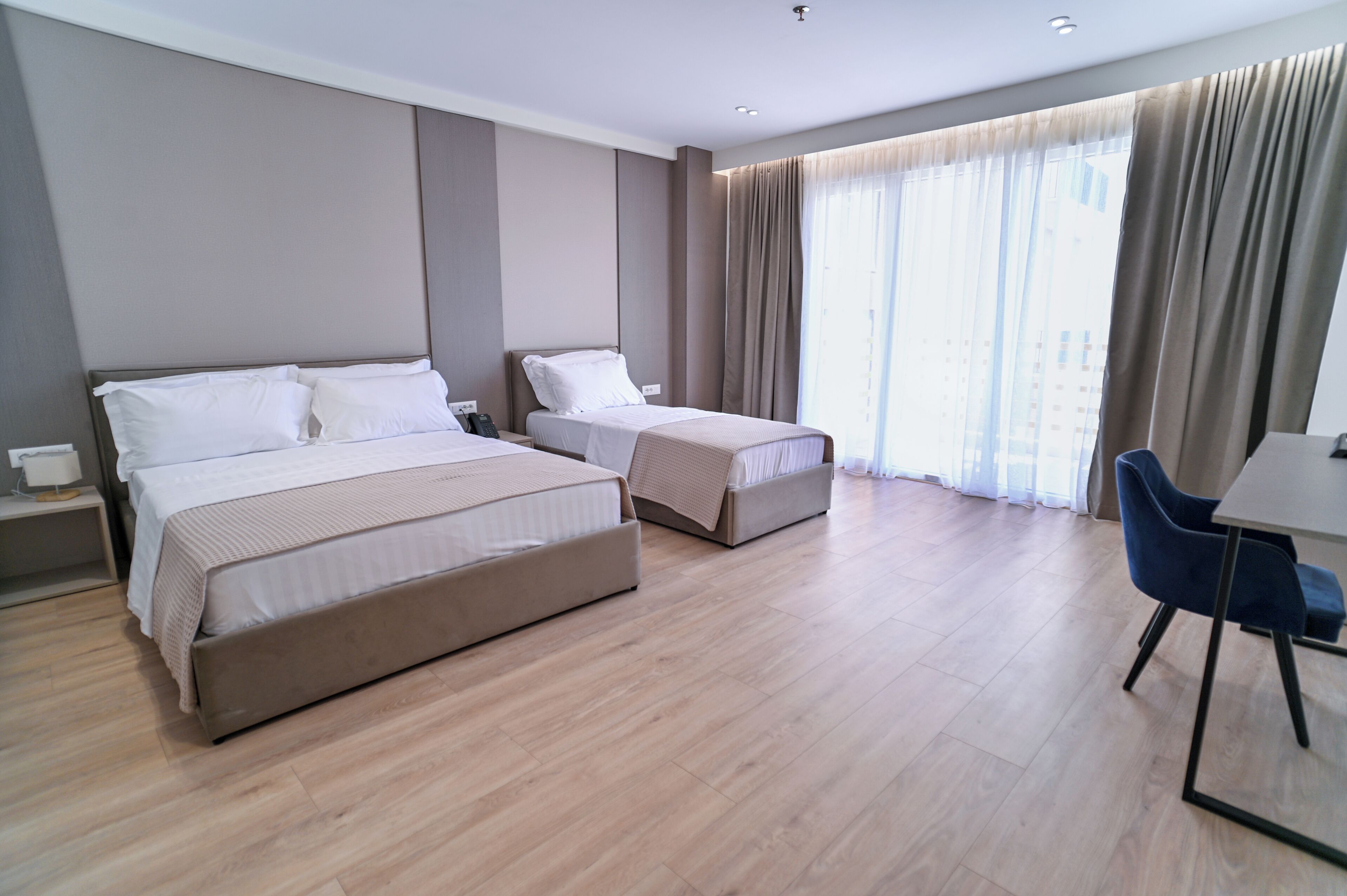 A modern hotel room with two beds, a desk, and a chair.