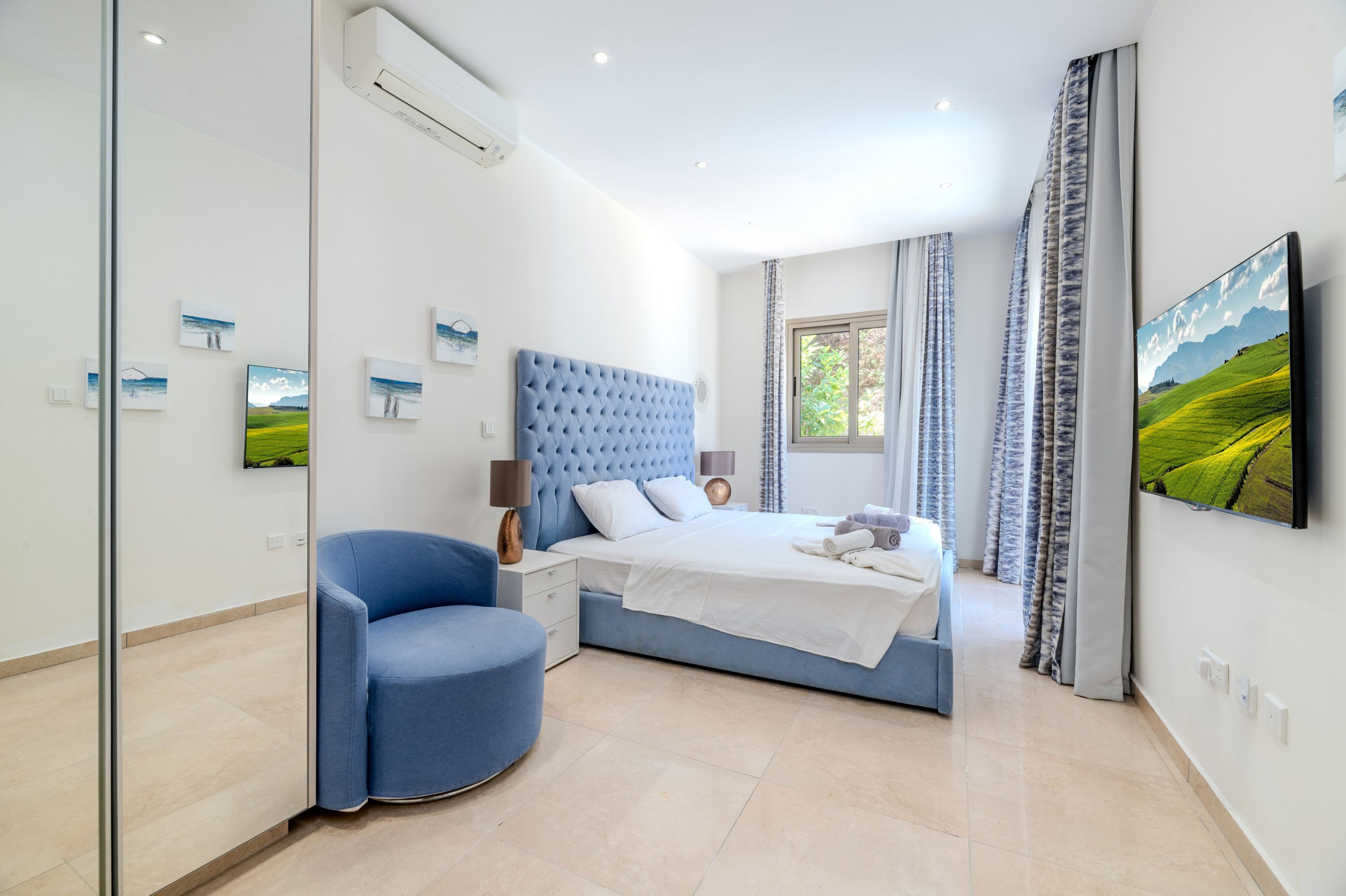 A bedroom with a bed, a chair, a nightstand, and a wall-mounted TV.