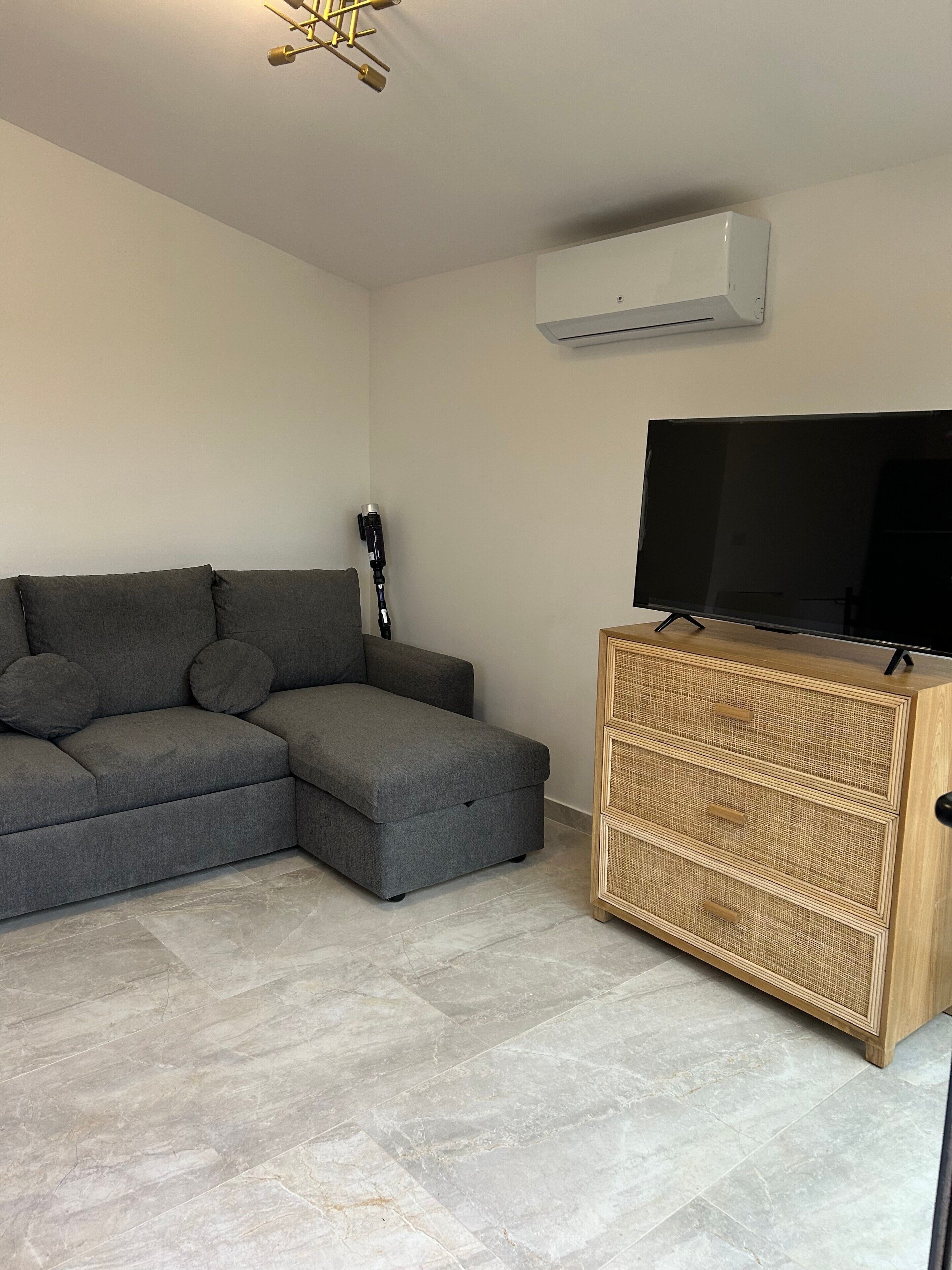 A living room with a sectional sofa, a flat-screen TV, a camera tripod, and a wicker cabinet.