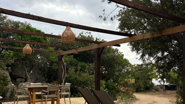Une terrasse en bois avec une table et des chaises, un fauteuil de relaxation et un luminaire suspendu.