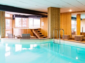 Ein Innenpool mit Holzwänden, einer Treppe und Sitzbereichen.