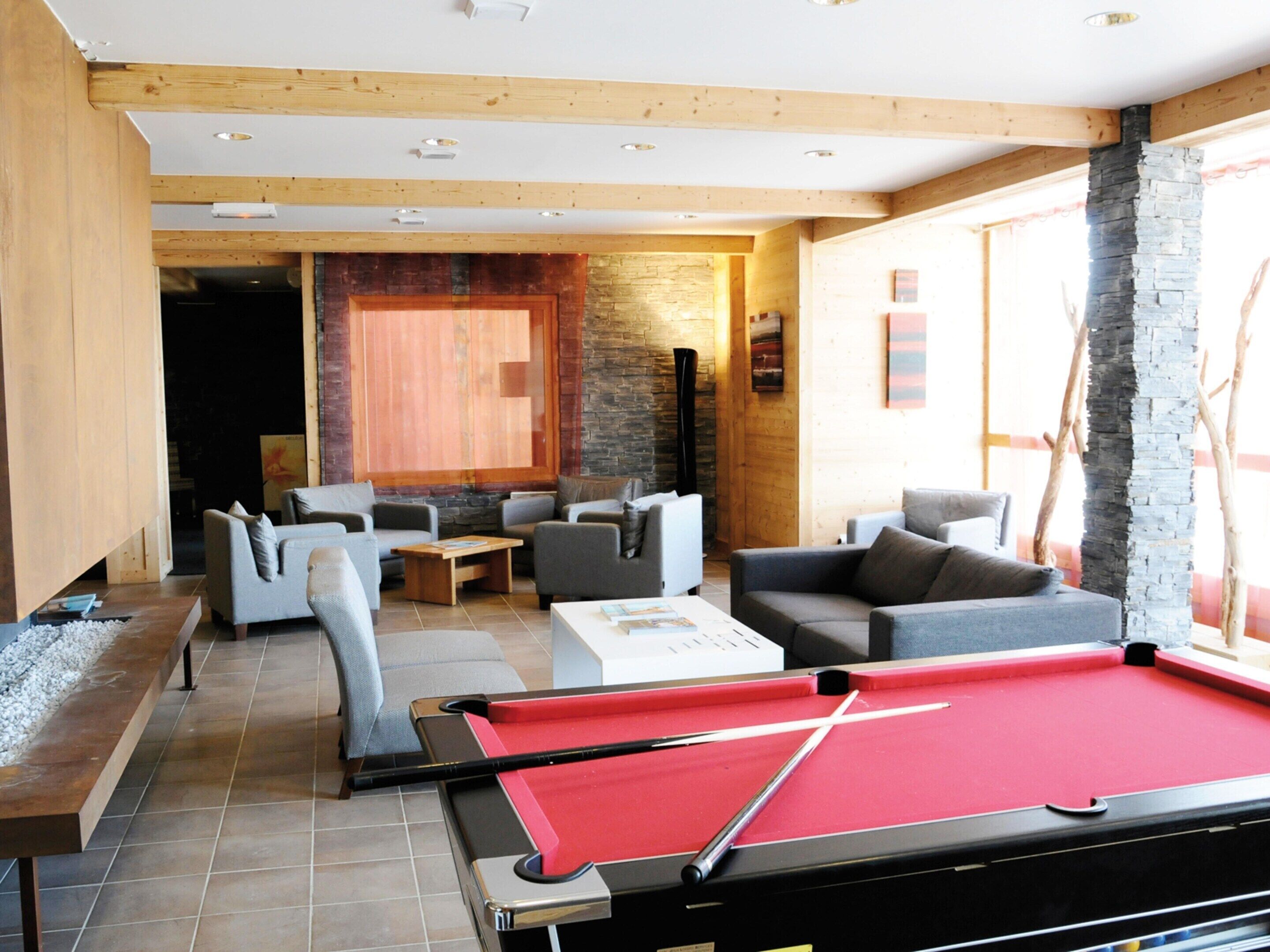 Un tavolo da biliardo in una zona relax moderna, con varie opzioni di seduta e una parete decorata in pietra.
