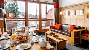 Una camera accogliente con un tavolo in legno apparecchiato per la colazione, un divano in pelle e ampie finestre che si affacciano sugli alberi.
